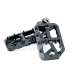 FactoryZ wide foot pegs for Surron e-moto, black CNC-machined aluminum pair with serrated grip teeth and skeletonized cutout platform