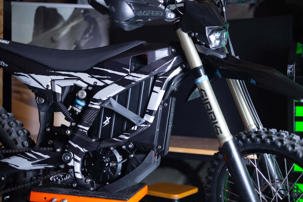 Surron Ultra Bee with EBMX XUB-80 motor, front-quarter view, black and white graphics, gold inverted fork and knobby tire