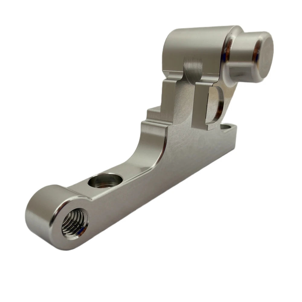 Surron front moto brake caliper bracket, CNC-machined silver aluminum, back-side angle showing mounting bores and threaded hole