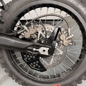 Surron Ultra Bee foot brake kit, black dual caliper bracket installed on the rear wheel, two OEM Surron calipers on one rotor