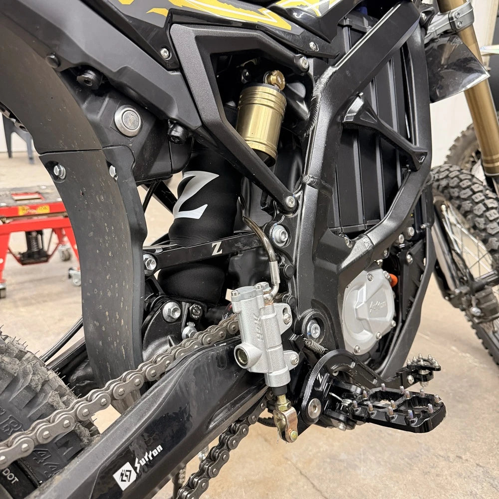 Surron Ultra Bee foot brake installed, side view, black Z logo bracket and peg, silver HSK master cylinder by the swingarm
