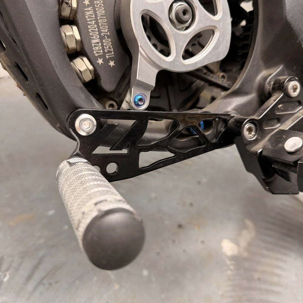 Talaria XXX shift lock kit installed, black CNC FactoryZ Z-cutout bracket with blue anodized bolts near belt-drive sprocket, close-up